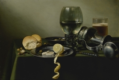 Still life with roemer, an overturned pewter jug, olives, and half-peeled lemon on pewter plates
